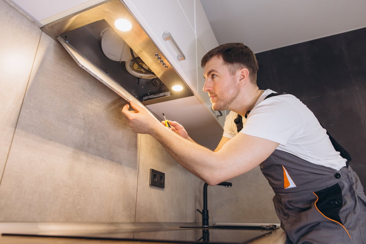 Professional plumber repairing an extractor fan in a modern kitchen, skillfully using a screwdriver for efficient maintenance and service