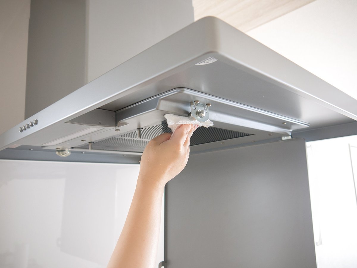 A woman is wiping the range hood with a tissue